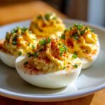 Four halves of classic deviled eggs, piped high with creamy filling, sprinkled with paprika and fresh chives.