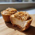Close-up of a cookie butter cheesecake cup cut in half, showing the creamy filling and cookie crust, topped with piped cookie butter.