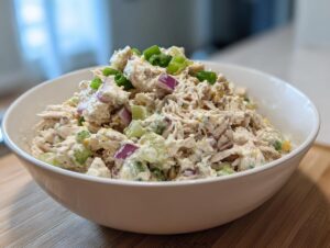 A white bowl filled with creamy cottage cheese chicken salad, mixed with diced red onion and celery, topped with green onions.