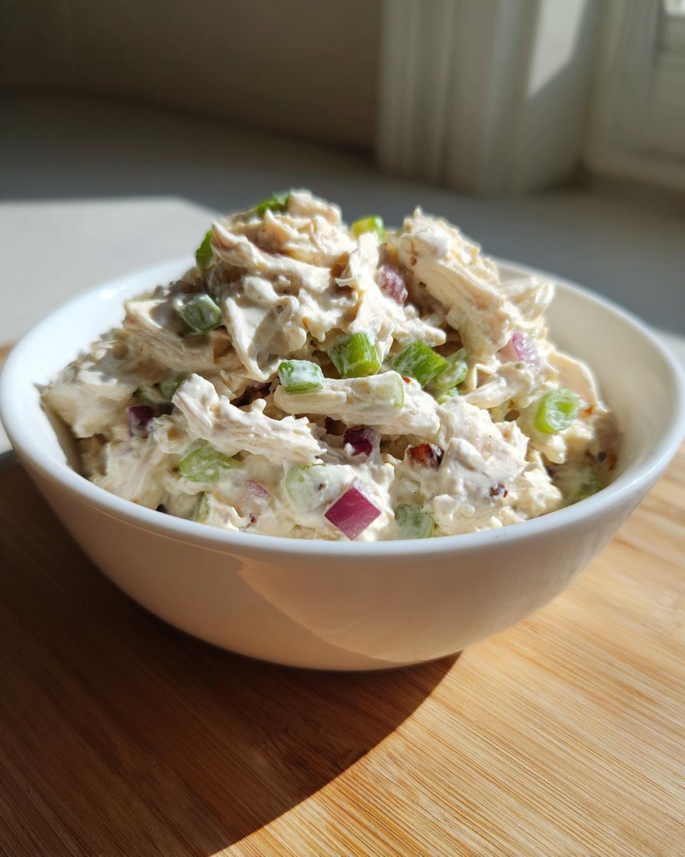 A white bowl filled with creamy cottage cheese chicken salad featuring shredded chicken, red onion, and green onions.
