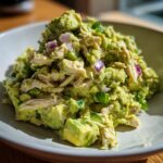 Close-up of a serving of creamy avocado chicken salad mixed with shredded chicken, chunks of avocado, and diced red onion.