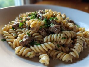 A close-up shot of creamy beef pasta featuring fusilli noodles coated in a light sauce and topped with ground beef and fresh parsley.