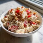 Close-up of a white bowl filled with creamy blt chicken salad featuring chunks of chicken, red tomatoes, and crispy bacon.