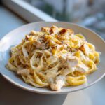 A close-up of a bowl filled with creamy chicken fettuccine alfredo, topped with black pepper.