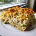 A generous slice of creamy chicken noodle casserole with shredded chicken, peas, and a golden-brown breadcrumb topping.
