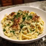 Close-up of creamy chicken pasta featuring fettuccine noodles, topped with seared chicken pieces and fresh parsley.
