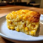 Close-up of a moist square slice of creamy corn side dish, studded with whole corn kernels.