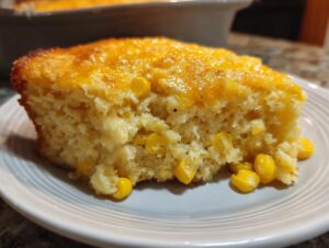 Close-up of a moist slice of creamy corn side dish, showing whole corn kernels embedded in the bread.