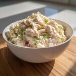A white bowl filled high with creamy cottage cheese chicken salad mixed with celery and red onion.