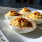 Four halves of creamy deviled eggs, generously piped with filling and sprinkled with paprika, served on a white plate.