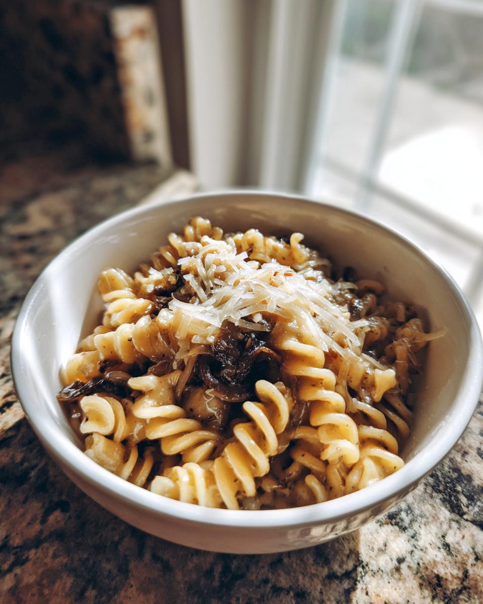 A white bowl filled with creamy french onion pasta (rotini) topped with shredded cheese.