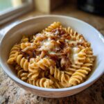 A close-up of creamy french onion pasta made with fusilli, topped with melted cheese and caramelized onions.