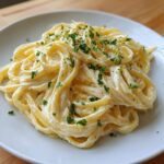 A close-up of a serving of creamy lemon pasta, coated in a rich sauce and topped with fresh parsley and lemon zest.