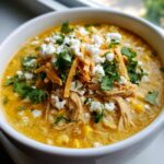 Close-up of a bowl of creamy mexican street corn soup topped with shredded chicken, cotija cheese, tortilla strips, and cilantro.
