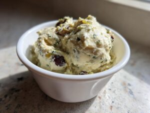 A close-up of a creamy, textured olive dip, featuring chunks of dark olives and green herbs, served in a small white bowl.
