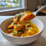 A spoonful of creamy pumpkin curry lifted from a white bowl, garnished with fresh cilantro.