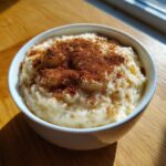 Close-up of a white bowl filled with creamy rice pudding generously dusted with cinnamon.