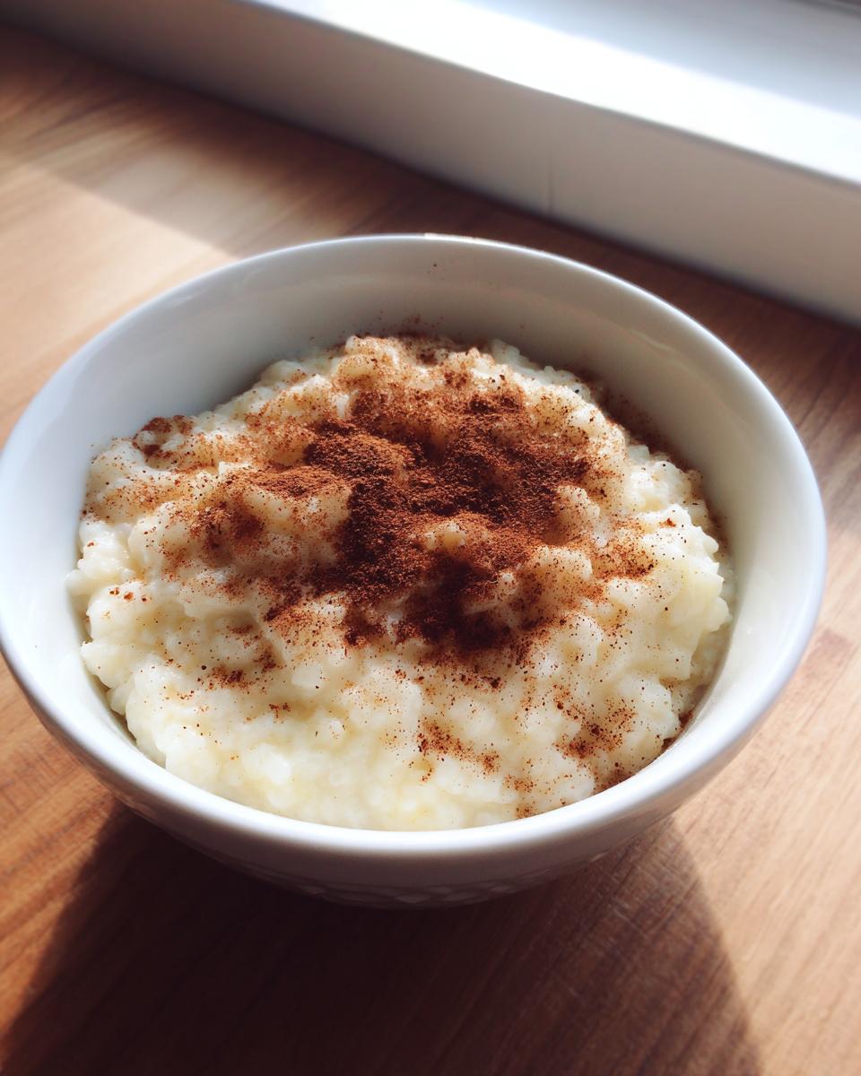 Close-up of creamy rice pudding in a white bowl, generously dusted with ground cinnamon.
