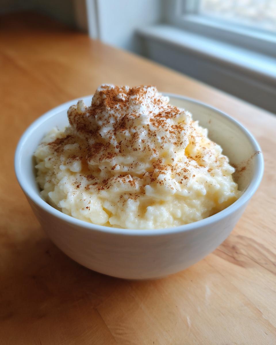 A white bowl filled with creamy rice pudding, topped with whipped cream and a dusting of cinnamon.