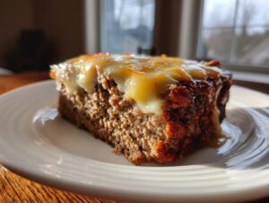 A close-up, sunlit slice of crockpot french onion meatloaf topped with melted Swiss cheese on a white plate.