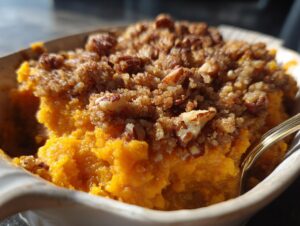 A close-up shot of creamy crockpot sweet potato casserole topped with a brown sugar and pecan crumble.