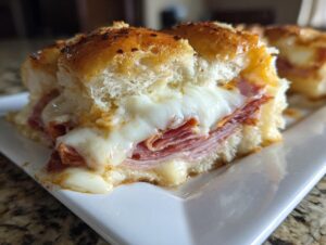 Close-up of a delicious grinder slider showing melted white cheese oozing over layers of deli meat on a toasted bun.