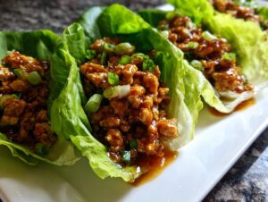 Close-up of several chicken lettuce wraps filled with savory ground chicken mixture and topped with green onions.