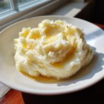 A close-up of fluffy garlic mashed potatoes in a white bowl, glistening with melted butter.