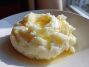A scoop of fluffy garlic mashed potatoes topped with melted butter pooling on a white plate.