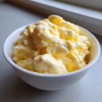 Close-up of creamy, fluffy scrambled eggs served in a small white bowl.