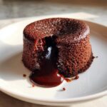 A single, rich chocolate lava cake with molten center oozing onto a white plate.