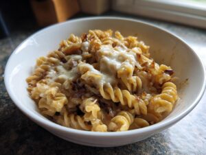 Close-up of a white bowl filled with creamy french onion pasta topped with melted white cheese and caramelized onions.