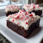 Close-up of a fudgy peppermint brownie square topped with thick white frosting and crushed candy canes.