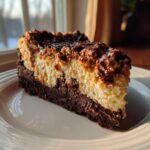 A decadent slice of german chocolate cheesecake featuring a dark brownie base and creamy filling topped with chocolate and nuts.