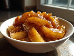A close-up view of glistening, spiced apple pie filling served in a small white bowl, highlighted by natural light.