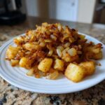 A mound of golden brown fried potatoes mixed with deeply caramelized onions served on a white plate.
