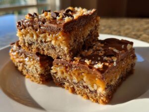 A stack of three rich, layered magic cookie bars topped with chocolate and coconut flakes.