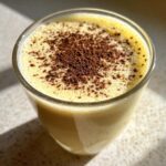 Close-up of a glass of creamy, frothy homemade eggnog topped with grated chocolate or nutmeg.
