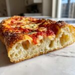 Close-up of a thick, airy slice of homemade pizza crust showing large air pockets and a cheesy tomato topping.