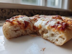 Close-up of a slice of homemade pizza showing the airy, thick crust and melted, stretching mozzarella cheese.