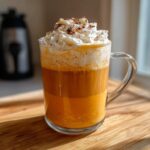 A vibrant, layered pumpkin spice latte topped with whipped cream and cinnamon, sitting on a wooden board.