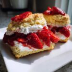 Two servings of homemade strawberry shortcake stacked high with whipped cream and fresh sliced strawberries.