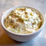 A close-up of thick, creamy tartar sauce loaded with chopped pickles and herbs, served in a small white bowl.