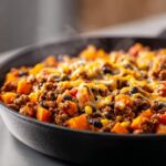 Close-up of a steaming sweet potato skillet featuring ground meat, black beans, corn, and melted cheese.