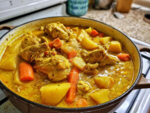 Close-up of rich, yellow Jamaican curry chicken stew with chunks of potato and carrot simmering in a Dutch oven.