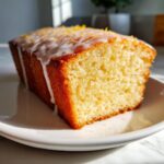 Close-up of a moist slice of lemon olive oil cake topped with white glaze and zest.