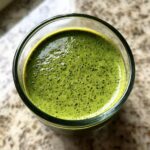 Overhead view of bright green matcha chia pudding with small dark specks in a clear glass.