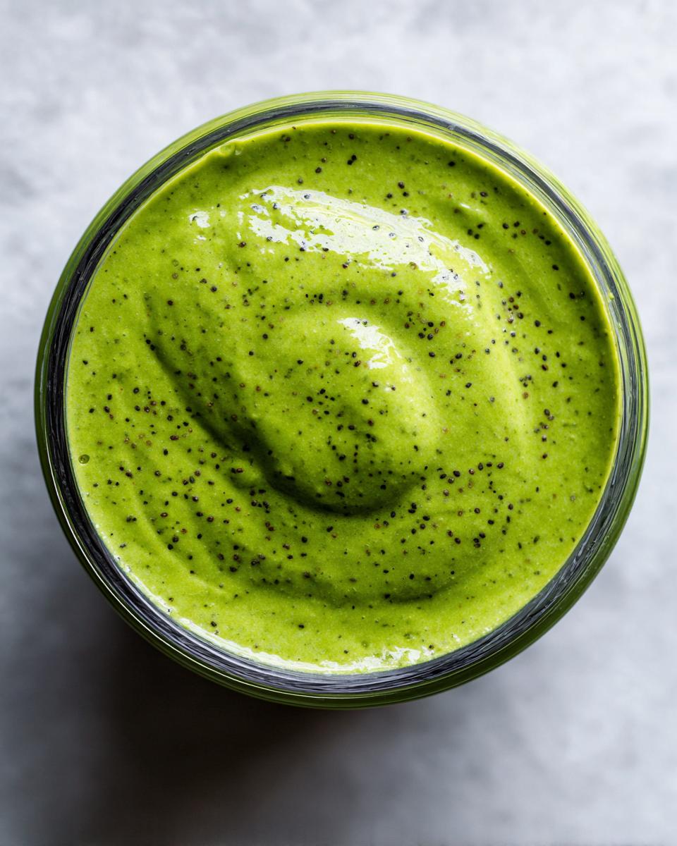 Overhead view of vibrant green matcha chia pudding speckled with black chia seeds in a glass jar.