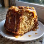 Close-up of a moist slice of apple dapple cake topped with thick caramel sauce dripping down the sides.