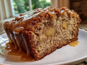 Close-up of a moist slice of apple dapple cake topped generously with a thick, dripping caramel sauce.